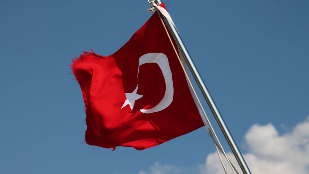 Red Turkish flag with crescent and star waving on a flagpole against a clear blue sky.
