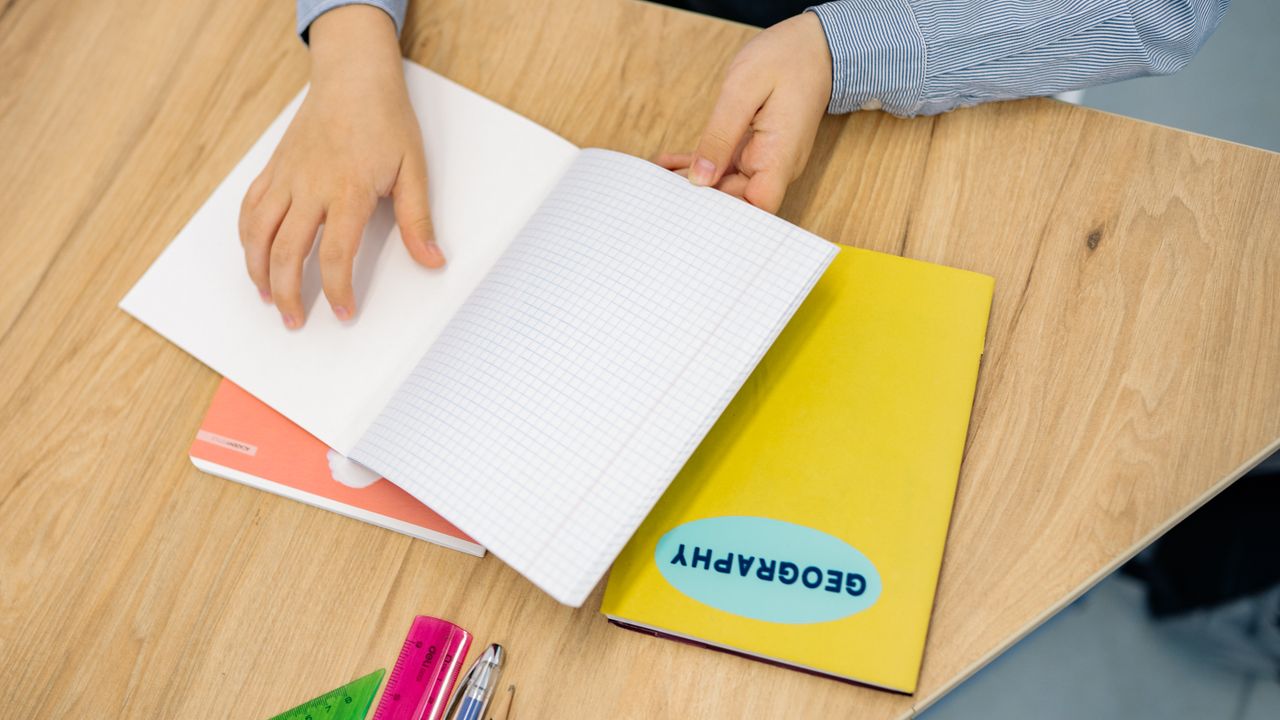 Hands flipping through a geography notebook on a wooden desk with pens and rulers.