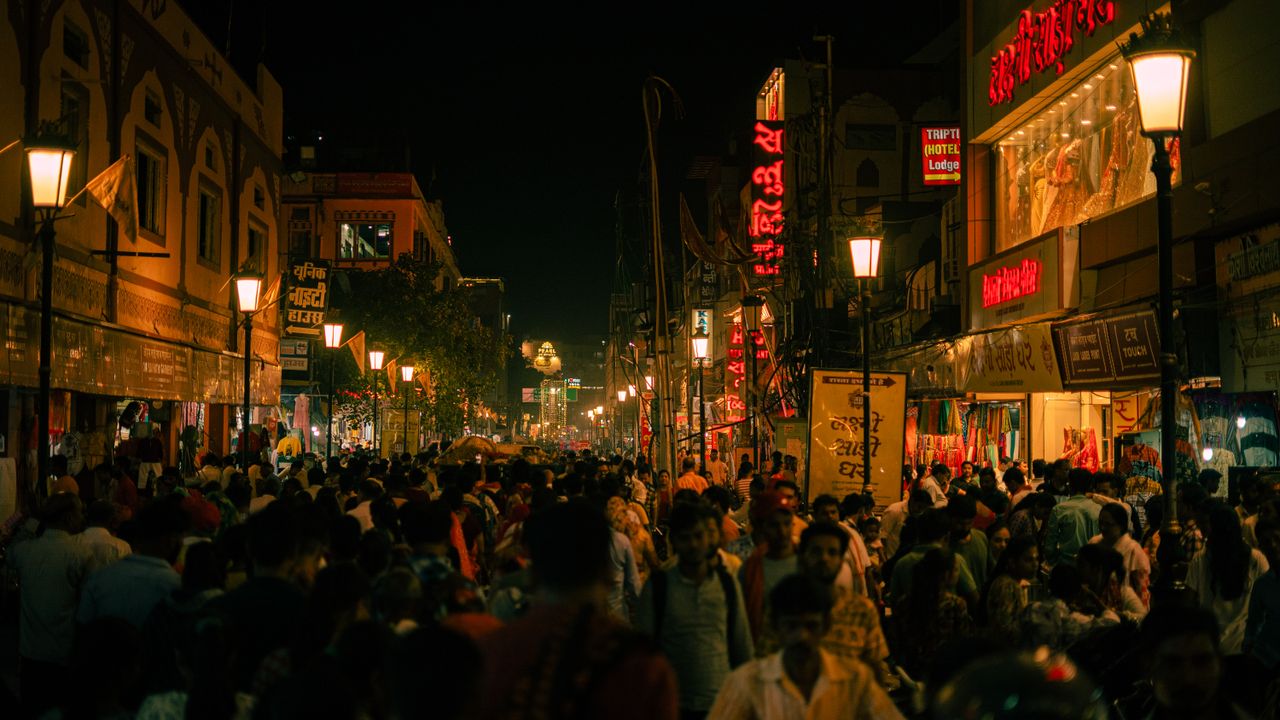 A bustling street in Varanasi, India, illuminated at night with crowds and vibrant signs.
