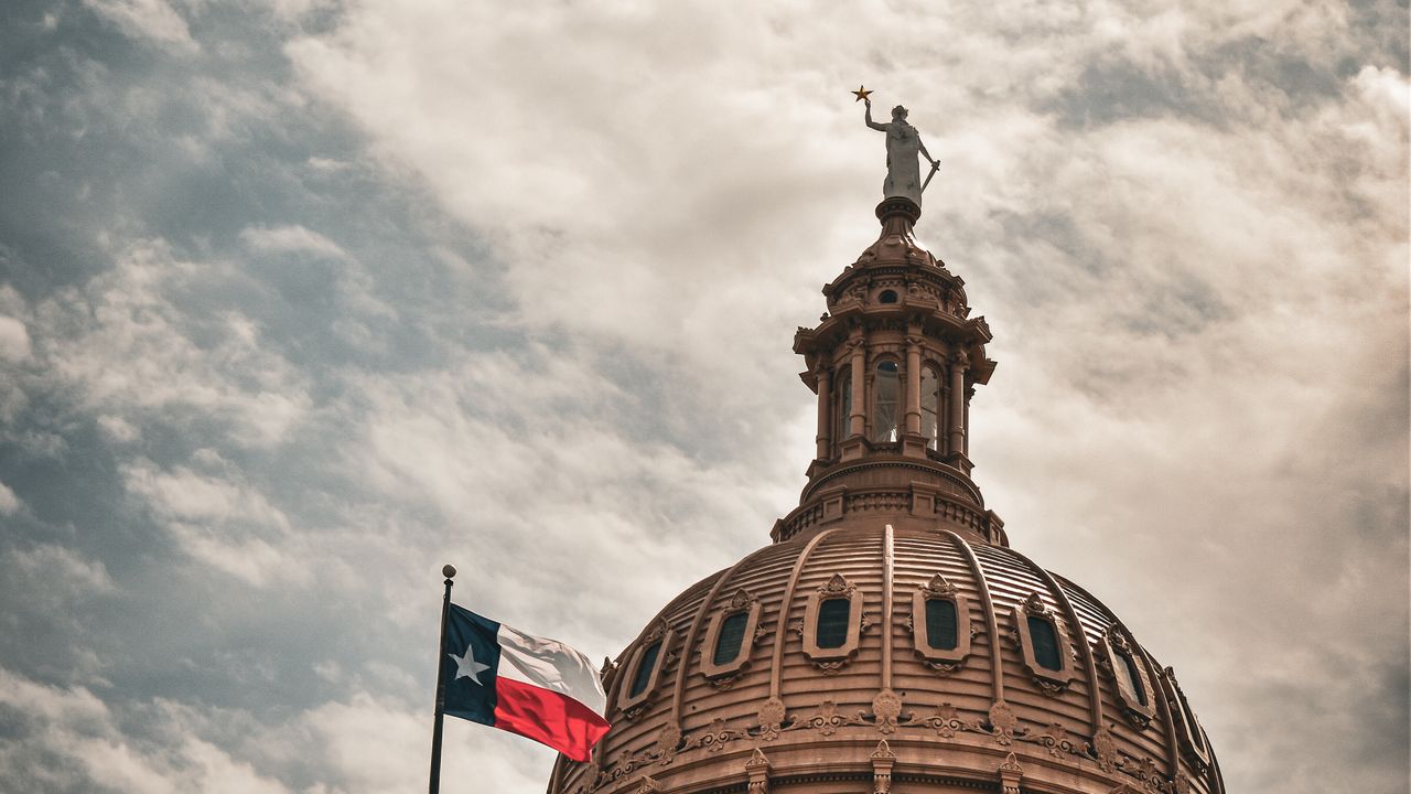 The Texas State Capitol dome in Austin, topped by the Goddess of Liberty, with the Texas flag flying.